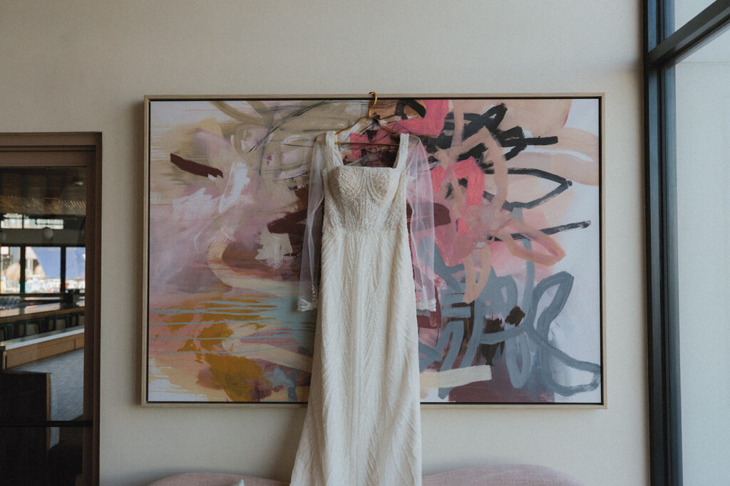 A wedding dress hangs before art work at a wave resort long branch wedding