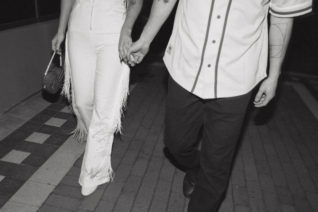 A black and white image depicts a couple holding hands as they walk down the sidewalk in Long Branch NJ before their wedding at The Wave Resort 