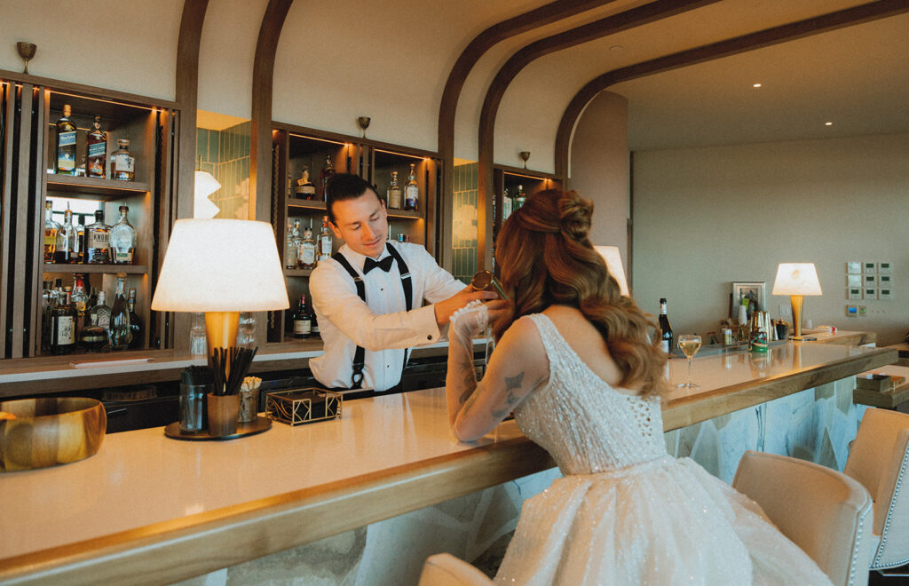 A groom pours a drink for his bride at the bar of The Wave Resort at their Long Branch New Jersey wedding 