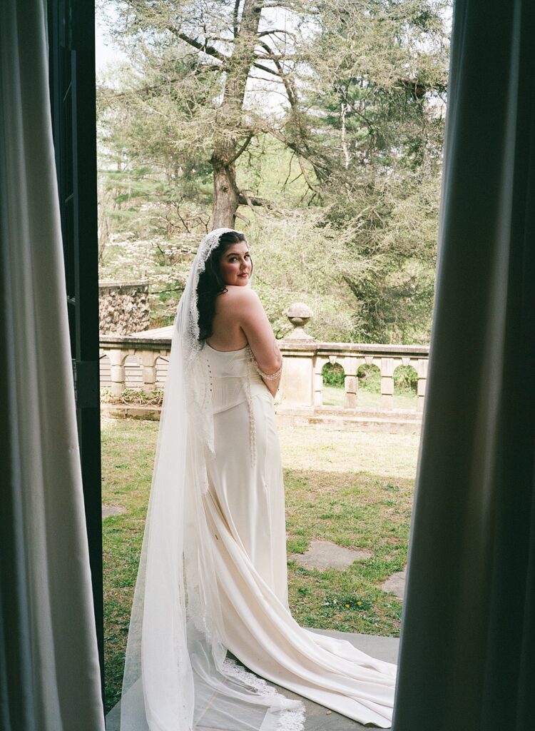 A bride looks over her shoulder in a photo taken at her ridley creek wedding
