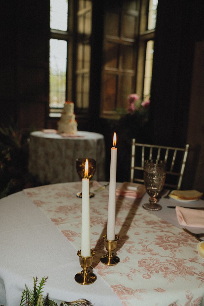 Tapered candles in brass holders set atop floral fabric are photographed at a reception held at ridley creek state park mansion
