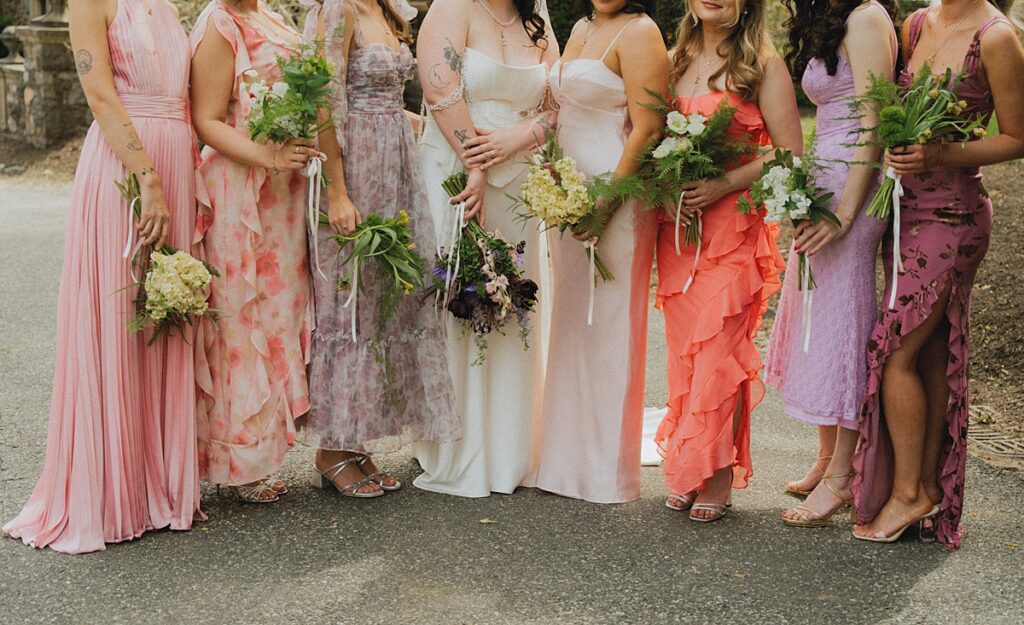 A photo taken at a ridley creek state park wedding showcase the bride and bridesmaids wearing dresses in shades of pink, coral, and purple