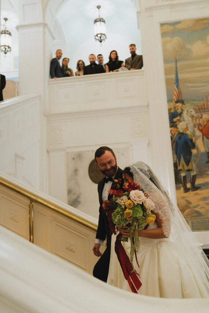 A bride and groom walk arm in arm up the grand staircase at their american swedish historical museum wedding